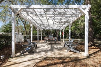 A white pergola with benches is set up in a park.